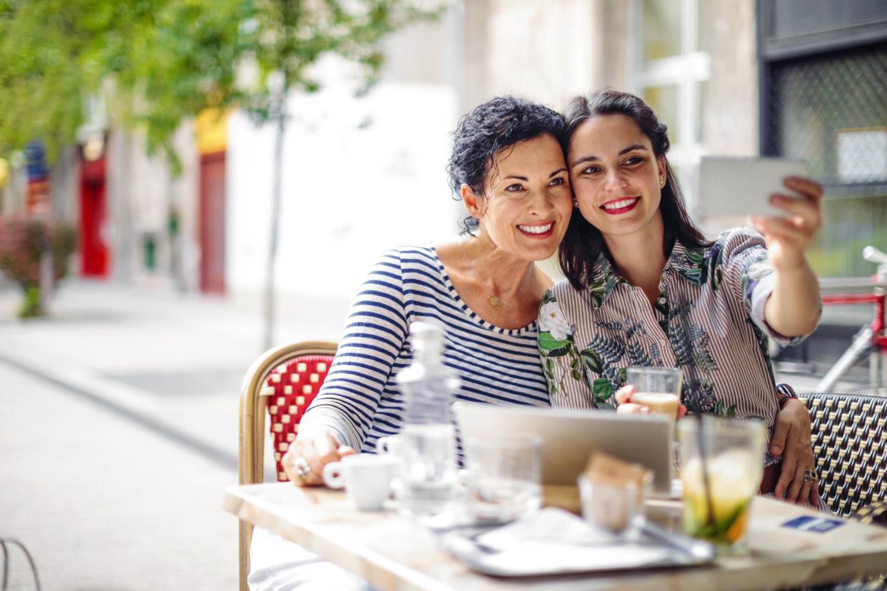 mother and daughter taking selfie while eating at outdoor restaurant