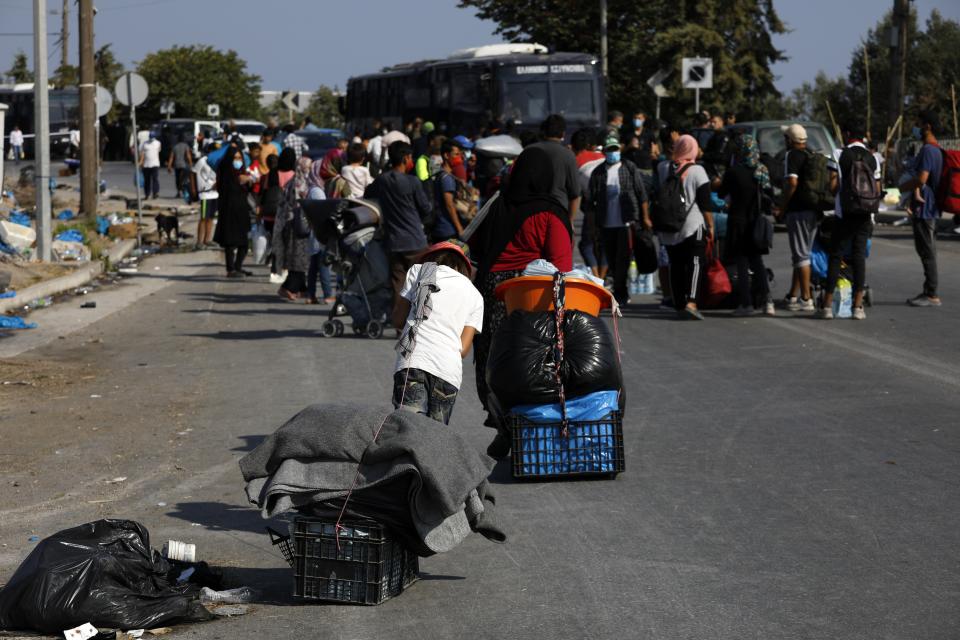 Migrants carry their belongings as they flee a road leading from Moria to the capital of Mytilene, on the northeastern island of Lesbos, Greece, Thursday, Sept. 17, 2020. A Greek police operation is underway on the island of Lesbos to move thousands of migrants and refugees left homeless after a fire destroyed their overcrowded camp, into a new facility on the island. (AP Photo/Petros Giannakouris)