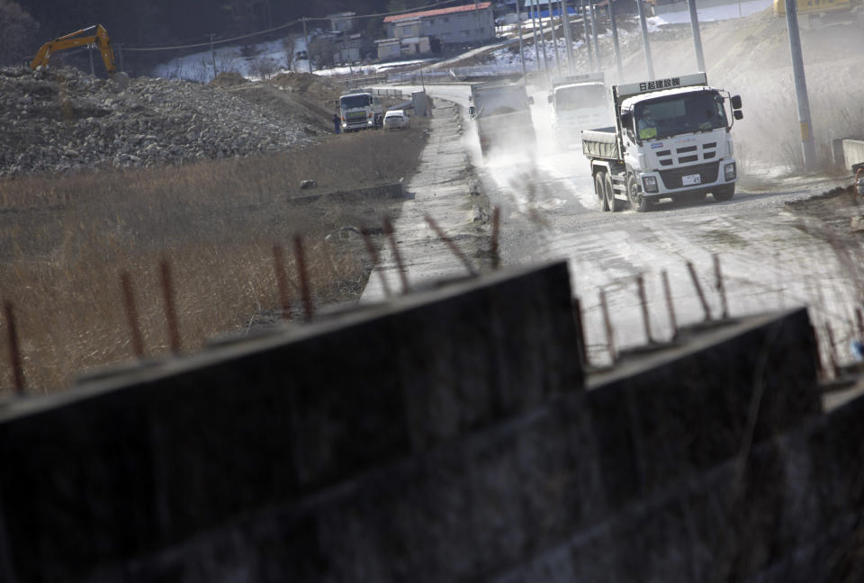 In this Tuesday, March 4, 2014 photo, dumpsters kick up clouds of dirt as they head to construction sites in Otsuchi, Iwate Prefecture, northeastern Japan. Construction has only begun at two of 10 planned sites in Otsuchi and further down the coast. (AP Photo/Junji Kurokawa)