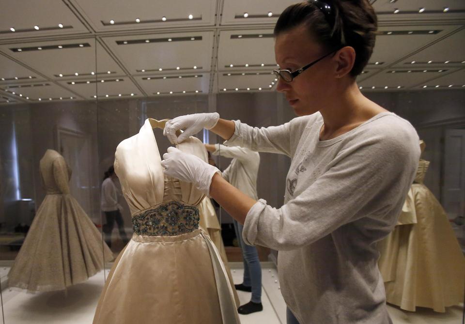 In this photo taken Monday July 1, 2013, an employee fixes a dress worn by Princess Margaret to a film premier in London and to a dinner in Paris as a guest of Prince Paul of Yugoslavia in 1951, at the Fashion Rules exhibition at Kensington Palace in London. Opening on 4 July, a new glamorous exhibit at Kensington Palace showcases how the styles of three royal ladies; Queen Elizabeth II, her sometimes risque sister Margaret, and the glamorous Princess Diana, each reflected and influenced the trends of their fashion heyday. (AP Photo/Frank Augstein)