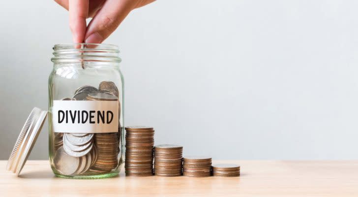 Hand putting coin in jar word dividend with money stack.