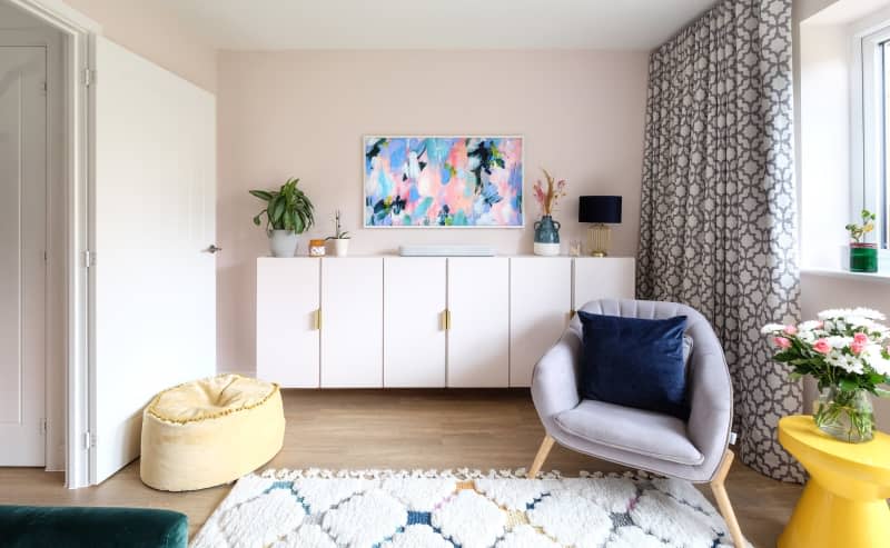 white tv console cabinet below colorful pastel frame tv with yellow modern side table and gray arm chair, white rug with pastel color diamond pattern and blue and white geometric pattern curtains