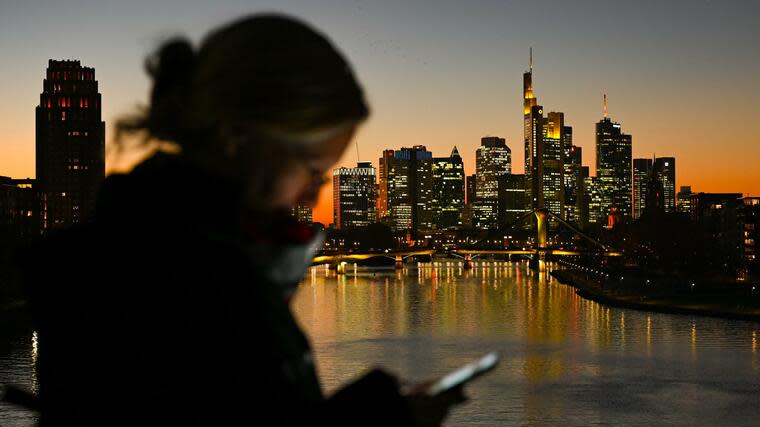 ARCHIV - 18.11.2020, Hessen, Frankfurt/Main: Eine Frau schaut auf ihr Smartphone während der Abendhimmel hinter den beleuchteten Hochhäusern der Frankfurter Skyline nach Sonnenuntergang in farbiges Licht getaucht ist. Die neue Social-Media-App Clubhouse stürmt an die Spitze der Download-Bestenliste. (zu dpa «Hype um Clubhouse: Audio-Social-Media-App überholt Telegram») Foto: Arne Dedert/dpa +++ dpa-Bildfunk +++ Foto: dpa