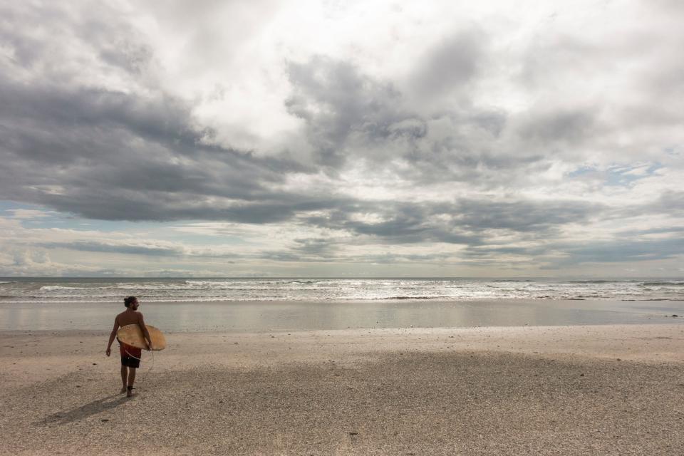 A surfer stands on the beach in front of the ocean. 