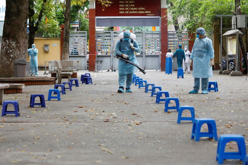 Health workers wearing protective suits spray disinfectant as a preventive measure against coronavirus at a makeshift rapid testing center for coronavirus disease (COVID-19), in Hanoi