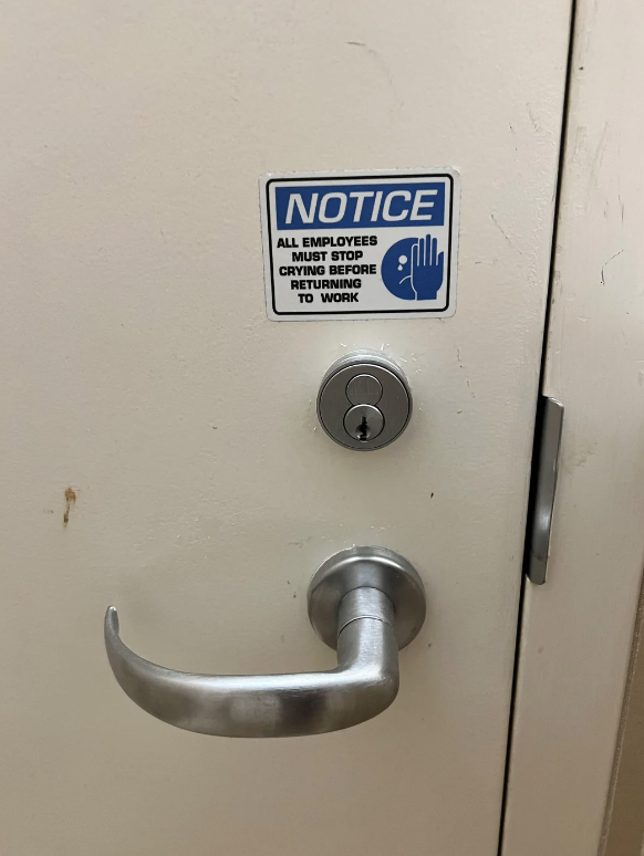 A door with a silver handle and a lock has a humorous notice sign that reads: "NOTICE: All employees must stop crying before returning to work."