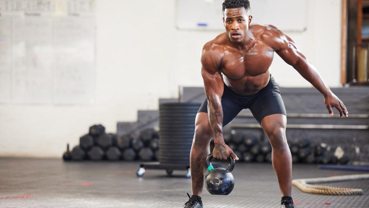  Man lifting a heavy kettlebell using right arm in a half squat position during gym workout. 