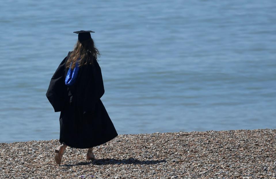 A woman wearing a 'mortar board' hat walks on the beach, following a graduation ceremony for students at University of Brighton, in Brighton, southern Britain, August 3, 2018. (Photo: REUTERS/Toby Melville)