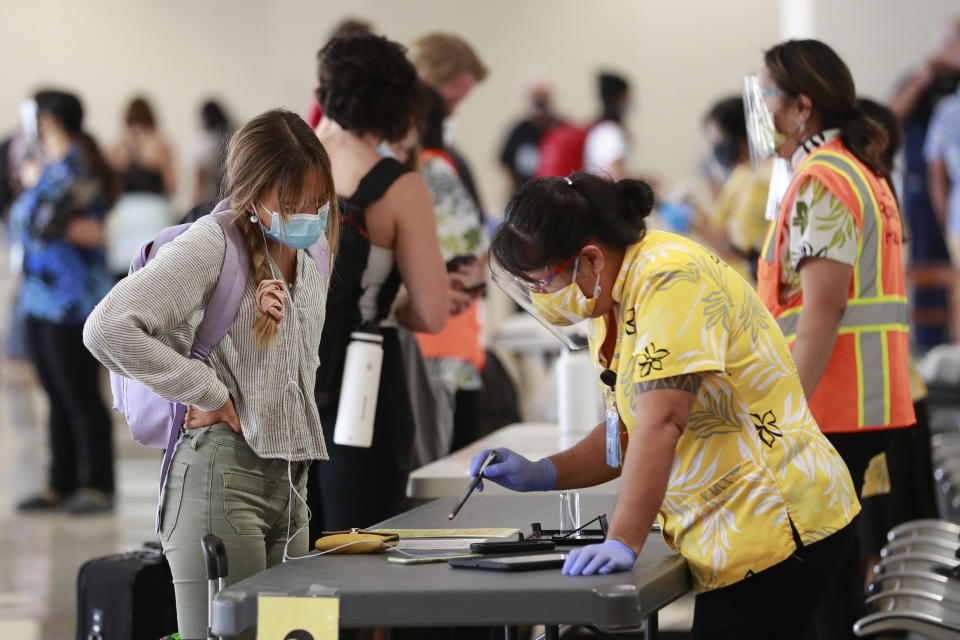 A traveler is assisted by a state official at the Daniel K. Inouye International Airport Thursday, Oct. 15, 2020, in Honolulu. A new pre-travel testing program will allow visitors who test negative for COVID-19 to come to Hawaii and avoid two weeks of mandatory quarantine goes into effect Thursday. The pandemic has caused a devastating downturn on Hawaii's tourism-based economy. Coronavirus weary residents and struggling business owners in Hawaii will be watching closely as tourists begin to return to the islands. (AP Photo/Marco Garcia)