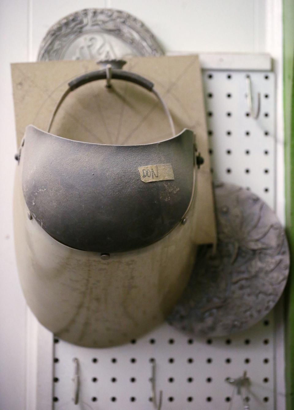 A dusty face shield labeled "Don" hangs on a wall in Don Drumm's workshop in Akron May 1.
