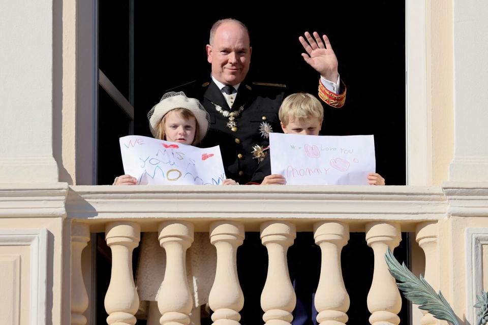 Prince Albert II of Monaco, Princess Gabriella and Prince Jacques stand with a message for Princess Charlene at the balcony of Monaco Palace