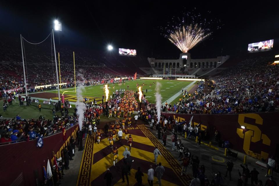 USC football players enter the field at night while fireworks go off.