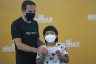 Eight-year-old Indigenous youth Davi Seremramiwe Xavante shows his COVID-19 vaccination card, alongside the Governor of Sao Paulo Joao Doria, after getting a shot of the Pfizer vaccine during a vaccination campaign for children at the Hospital da Clinicas in Sao Paulo, Brazil, Friday, Jan. 14, 2022. The state of Sao Paulo started the COVID-19 vaccination of children between ages 5 and 11. (AP Photo/Andre Penner)