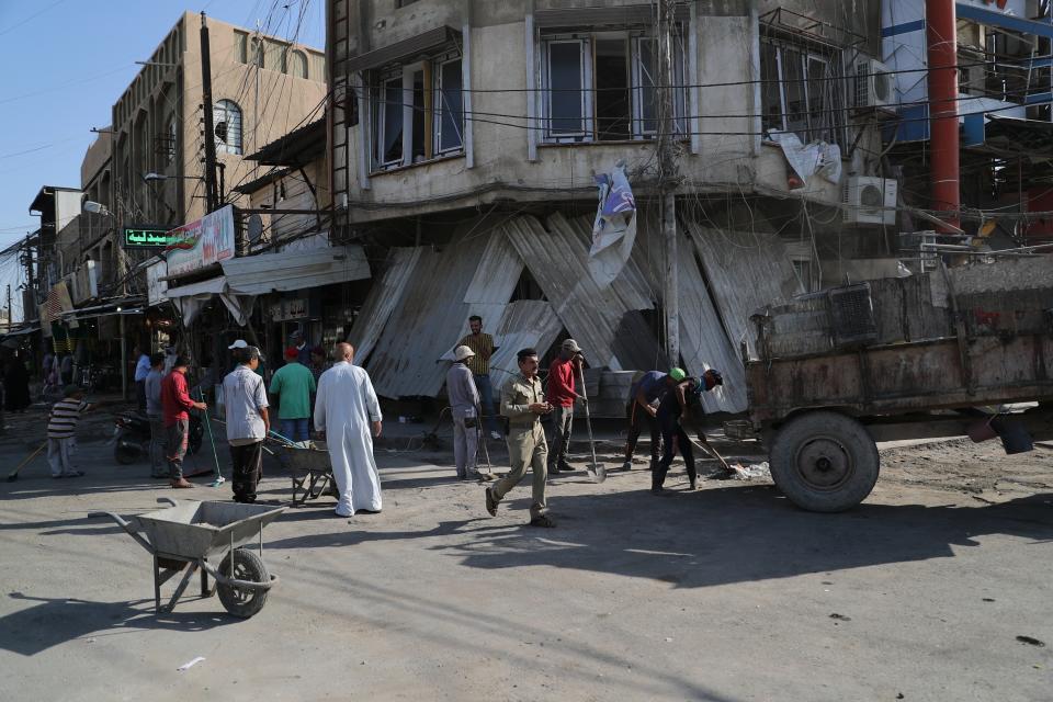 Municipality workers clean up as civilians inspect the aftermath a day after a motorcycle rigged with explosives exploded in Mussayyib, south of Baghdad, Iraq, Saturday, Aug. 24, 2019. The officials said Saturday that the blast occurred the previous evening on a commercial street in the village of Mussayyib, killing and wounding civilians. (AP Photo/Khalid Mohammed)