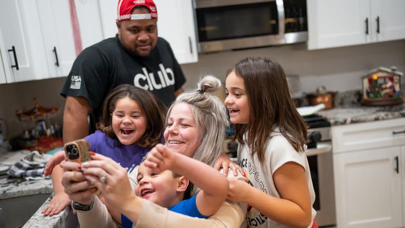 Maka Palu, back, looks on as his wife, Jessica Palu, and three of their children, Lini, 5; Bubba, 4; and Fine, 7, look at a video on her phone at their home in Eagle Mountain on Tuesday, Nov. 28, 2023.