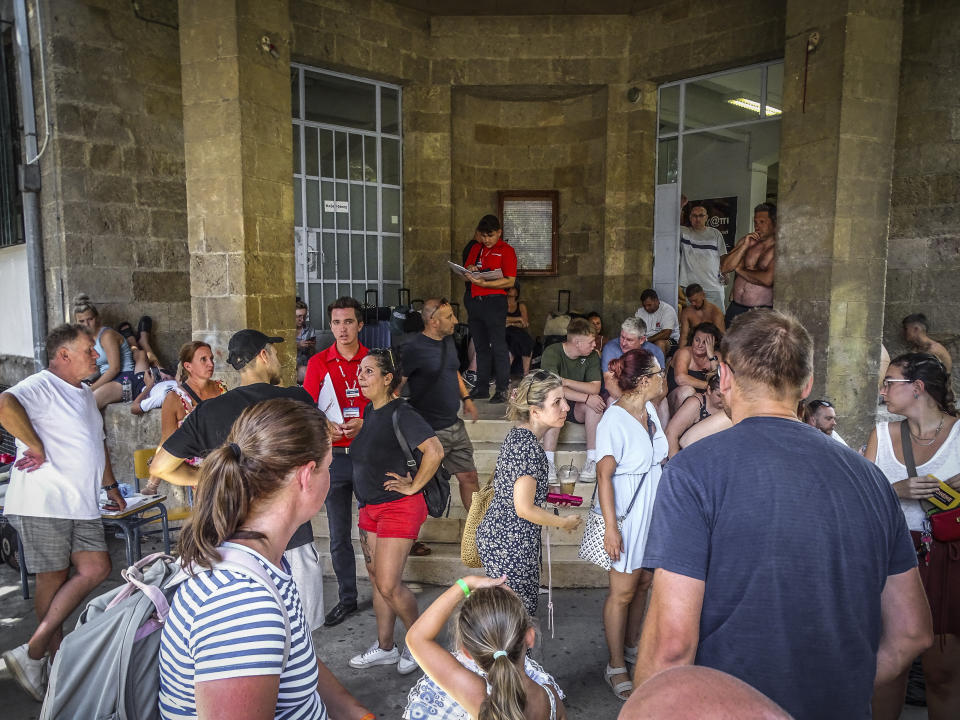 Evacuees gather outside a building following their evacuation during a forest fire on the island of Rhodes, Greece, Sunday, July 23, 2023. Some 19,000 people have been evacuated from the Greek island of Rhodes as wildfires continued burning for a sixth day on three fronts, Greek authorities said on Sunday. (Argyris Mantikos/Eurokinissi via AP)