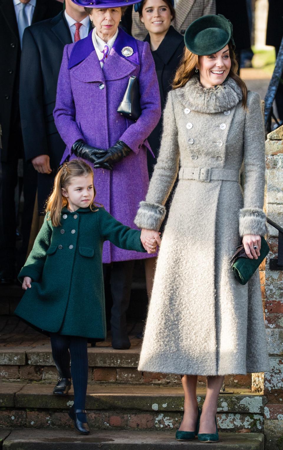 Princess Charlote and Kate Middleton stand together on a set of stone steps with other members of the royal family behind them.