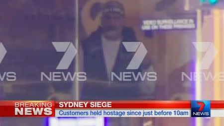 A man is seen standing behind the window of the Lindt cafe, where hostages are being held, in this still image taken from video from Australia's Seven Network on December 15, 2014. REUTERS/Reuters TV via Seven Network/Courtesy Seven Network