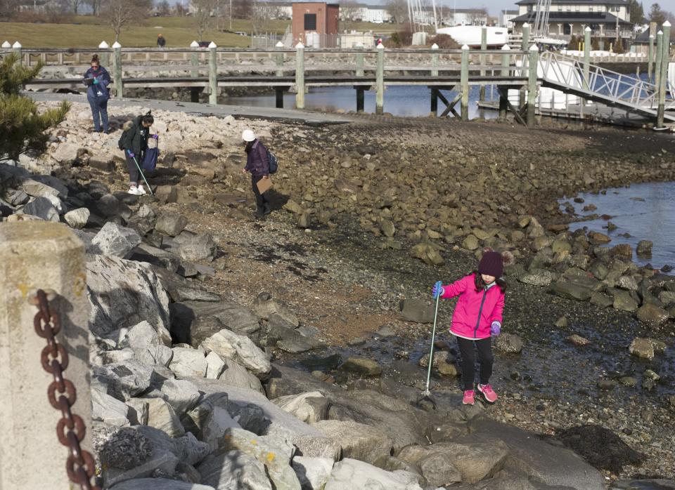 Children and adults walk the shoreline looking for litter during a 2020 beach clean up at Fort Adams State Park.