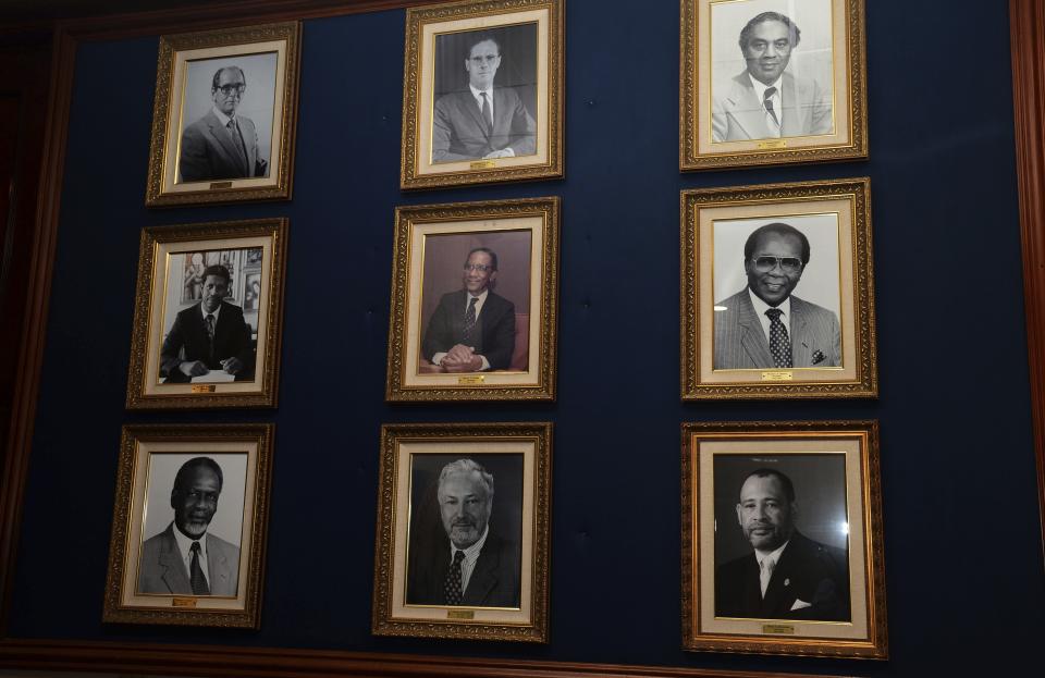 In this June 13, 2019 photo, framed photos of former Bank of Jamaica governors adorn a wall at the bank in Kingston, Jamaica. The central bank focused on using exchange rate adjustments to keep prices of goods and services neither too low nor too high, but that resulted in swings that made it difficult for businesses to plan. The bank now makes monetary decisions based on inflation, seeking a moderate but steady rise in prices. (AP Photo/Collin Reid)