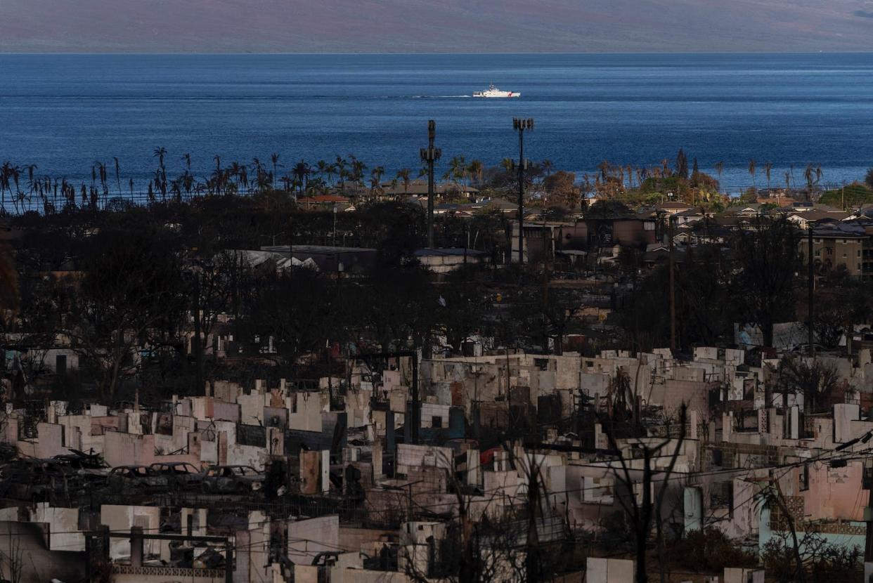 A general view shows the aftermath of a wildfire in Lahaina, Hawaii, Wednesday, Aug. 16, 2023, as a Coast Guard vessel sails through the ocean past the devastated community. Long before a wildfire blasted through the island of Maui the week before, there was tension between Hawaii's longtime residents and the visitors some islanders resent for turning their beaches, mountains and communities into playgrounds. But that tension is building in the aftermath of the deadliest U.S. wildfire in more than a century. (AP Photo/Jae C. Hong)