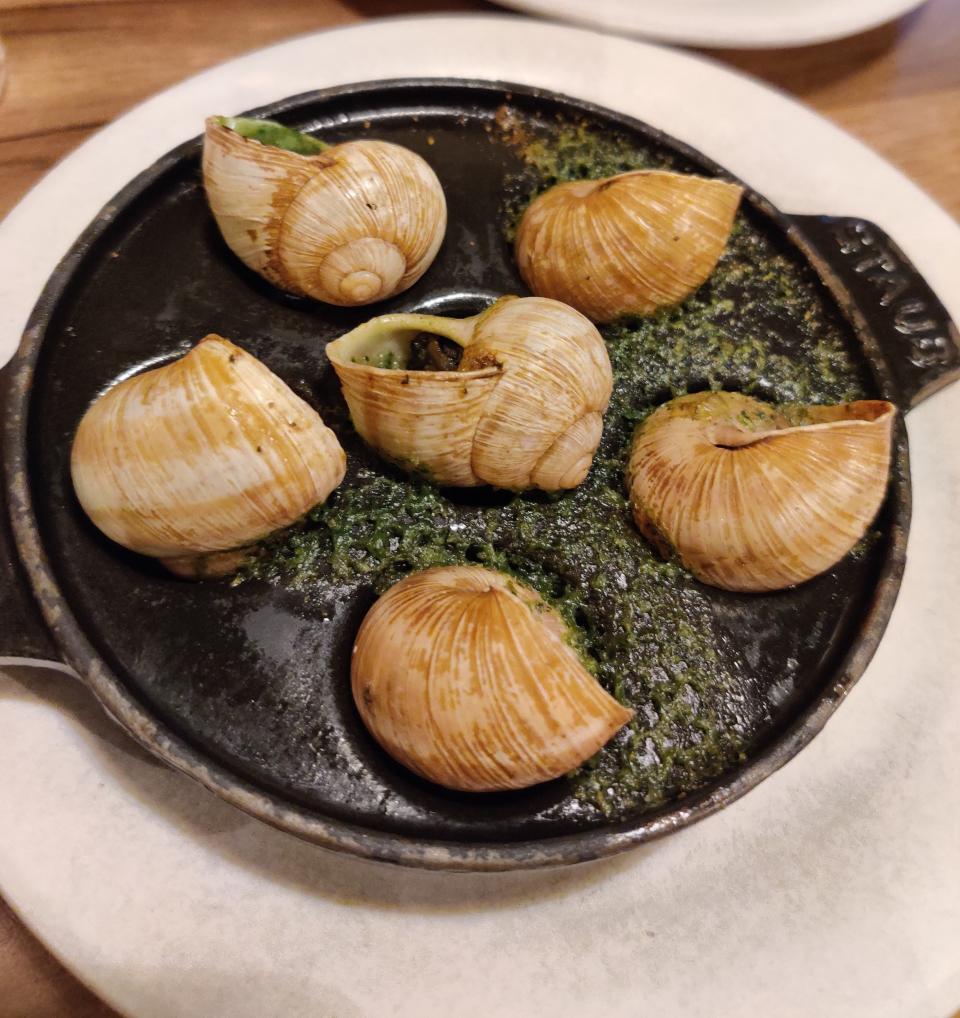 A plate of escargot cooked with garlic and herb butter, served in a round dish on a white plate