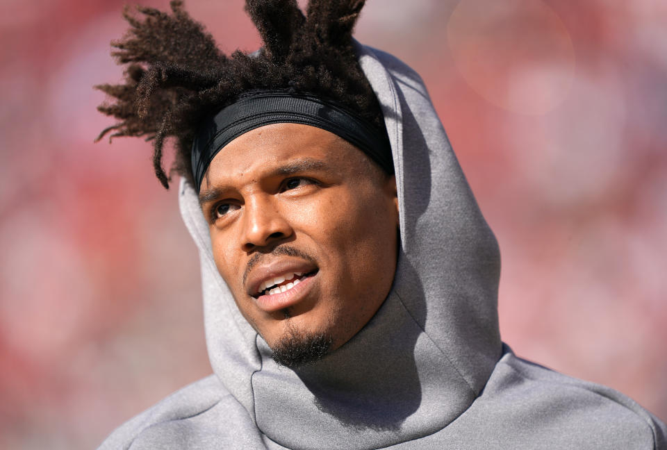 Cam Newton wears a hoodie on the sideline during a game.