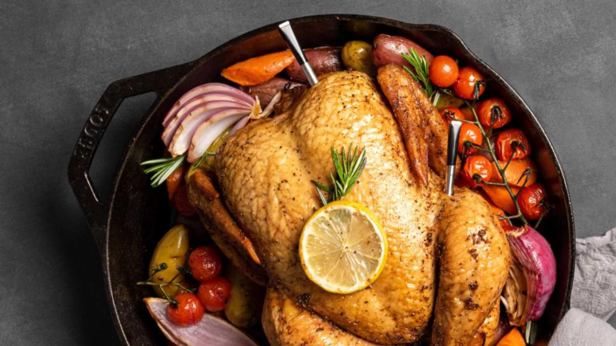  A roast chicken sat on vegetables with two meat thermometers inside it. 