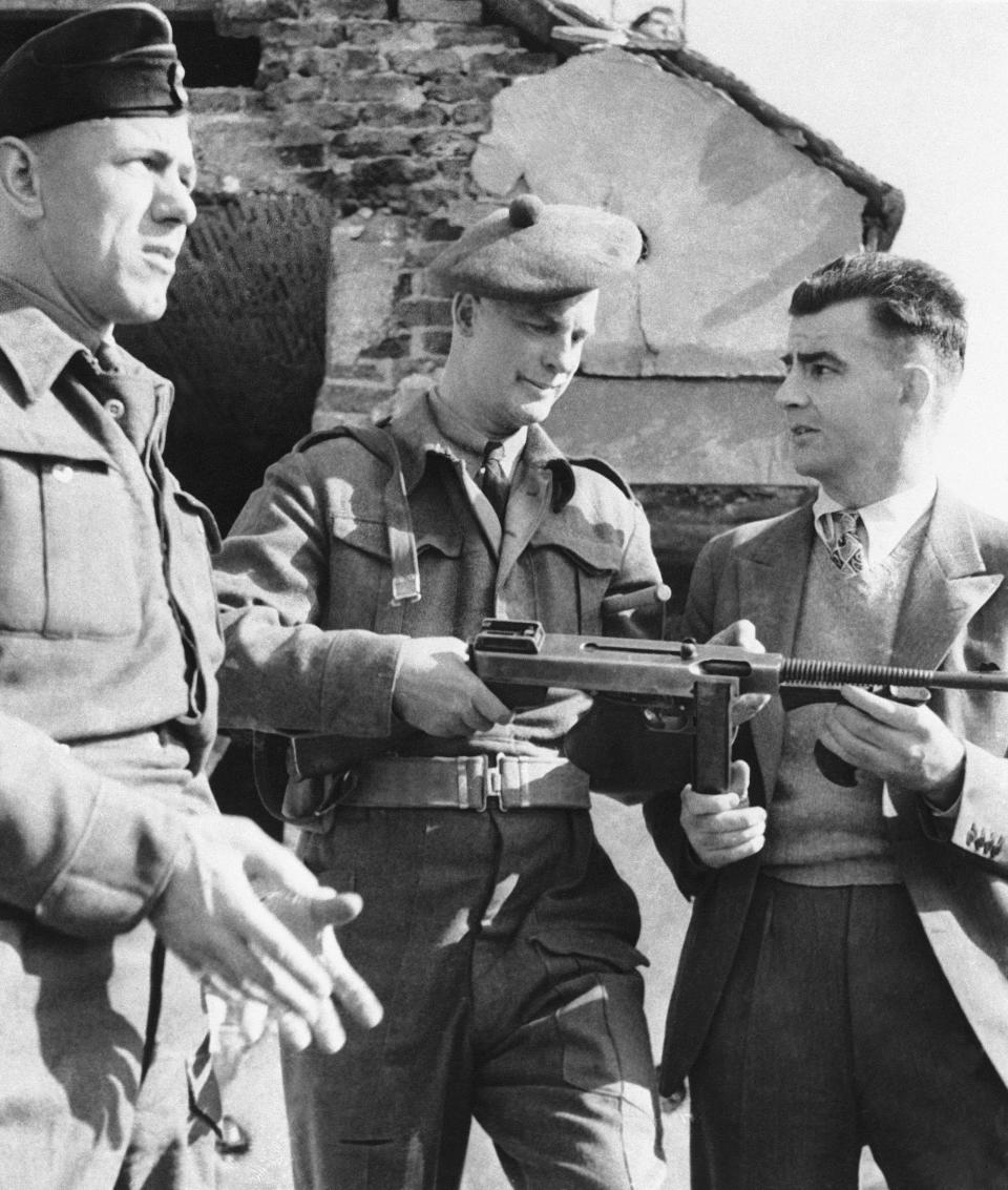 FILE - Associated Press war correspondent J. Wes Gallagher, right, is shown a Thompson submachine gun by Major J.S.P. Armstrong, center, commander of the Canadian Army's Commando School, June 10, 1942. On D-Day morning, June 6, 1944, The Associated Press had reporters, artists and photographers in the air, on the choppy waters of the English Channel, in London, and at English departure ports and airfields. Veteran war correspondent Wes Gallagher directed AP's team from the headquarters in Portsmouth, England, of Supreme Allied Commander Gen. Dwight D. Eisenhower. (AP Photo, File)