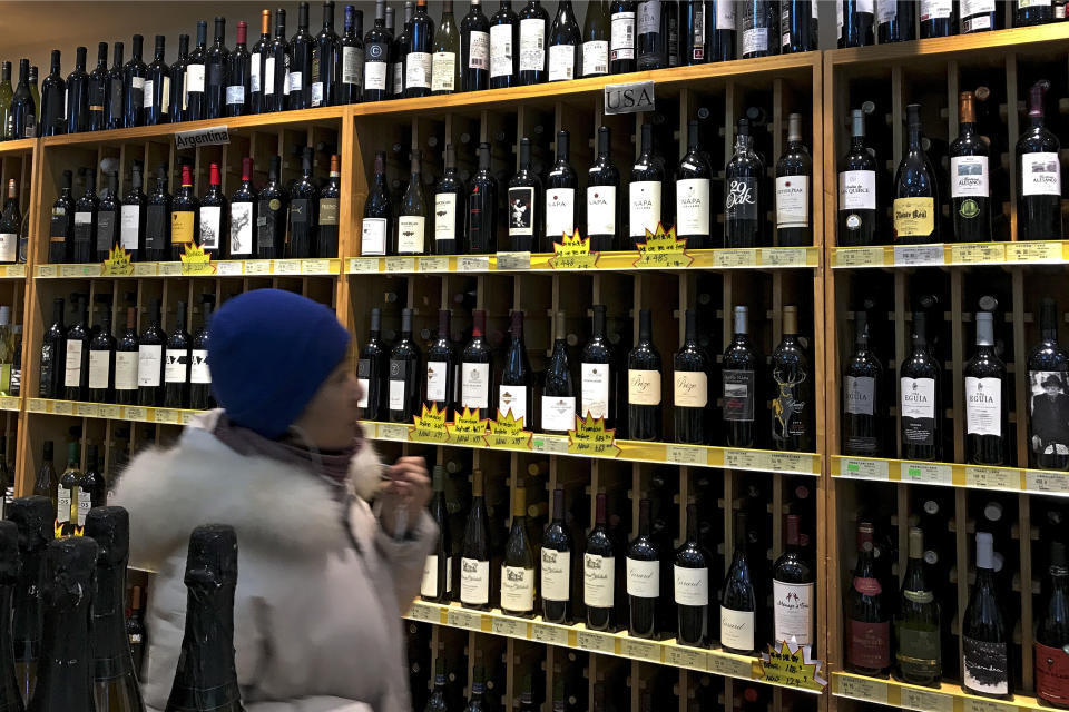 A woman walks by a shelve displaying bottles of American wine for sale at a supermarket in Beijing, Tuesday, Dec. 11, 2018. China's economy czar and the U.S. Treasury secretary discussed plans for talks on a tariff battle, the government said Tuesday, indicating negotiations are going ahead despite tension over the arrest of a Chinese tech executive. (AP Photo/Andy Wong)