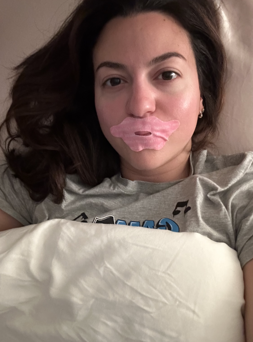 Woman lying in bed with a lip-shaped beauty mask on her lips