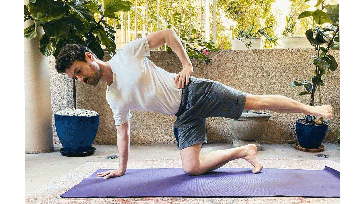 Man kneeling on a yoga mat with his left leg lifted and his right hand on the mat practicing Half Moon Pose