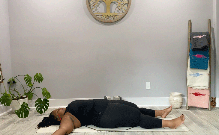 Woman lying on yoga mat with her legs and arms extended in the yoga pose Savasana