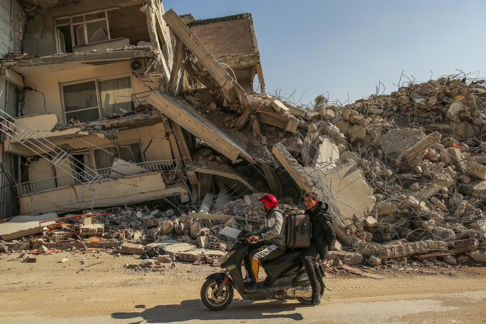 Men ride a motorcycle past destroyed buildings in Samandag, southern Turkey, Wednesday, Feb. 22, 2023. Survivors of the earthquake that jolted Turkey and Syria 15 days ago, killing tens of thousands of people and leaving hundreds of thousands of others homeless, dealt with more trauma and loss Tuesday after another deadly quake and aftershocks rocked the region. (AP Photo/Emrah Gurel)