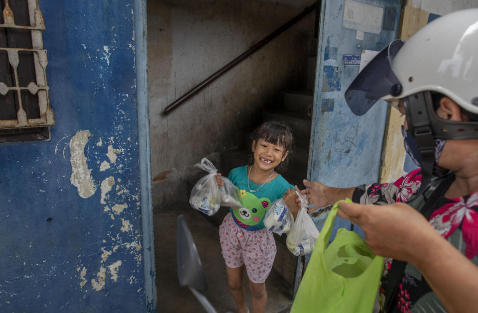 Ratthaphon Datwong, 6, smilies as she receives meals for her and her neighbors from her teacher Kanyarat Phuankuntod on Thursday, June 25, 2020 in Bangkok, Thailand. During the third month that schools remained closed due to the coronavirus outbreak, teachers have cooked meals, assembled food parcels and distributed them to families in this community sandwiched between an old railway line and a khlong, one of Bangkok’s urban canals. (AP Photo/Gemunu Amarasinghe)