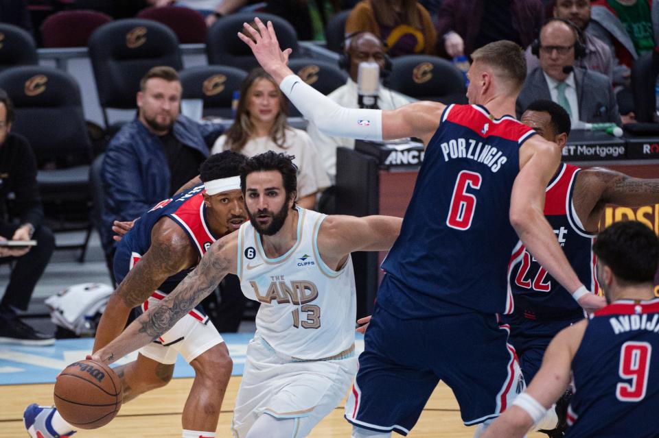 Cleveland Cavaliers' Ricky Rubio (13) drives past Washington Wizards' Kristaps Porzingis (6) and Bradley Beal, left, during the second half of an NBA basketball game in Cleveland, Friday, March 17, 2023. (AP Photo/Phil Long)