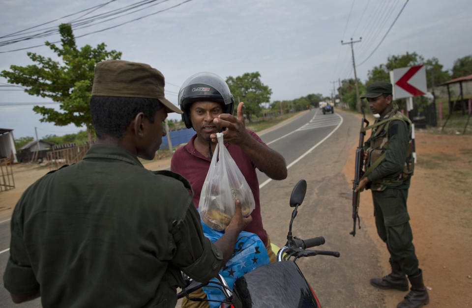 An army officer checks a bag belonging to a man on a motor bike at a roadside checkpoint in Kalmunai, Sri Lanka, Sunday, April 28, 2019. Police in Ampara showed The Associated Press on Sunday the explosives, chemicals and Islamic State flag they recovered from the site of one security force raid in the region as Sri Lanka's Catholics celebrated at televised Mass in the safety of their homes. (AP Photo/Gemunu Amarasinghe)