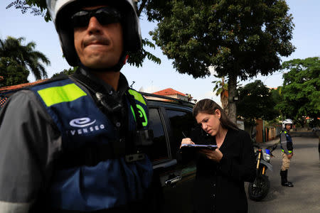 Vanessa Mikuski fills a form as employees of Pana, a mobile application which dispatches security crews to stranded drivers who request help, stand guard next to her in Caracas, Venezuela June 15, 2018. Picture taken June 15, 2018. REUTERS/Adriana Loureiro