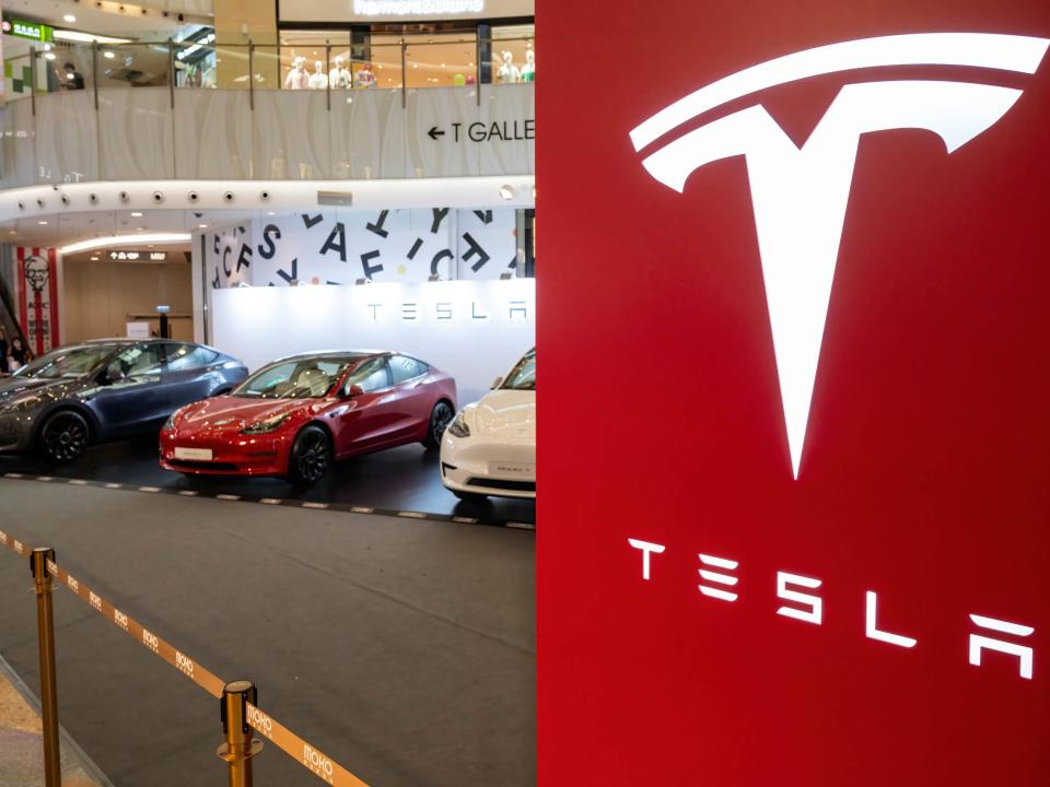 Photo of Tesla logo with cars seen behind it