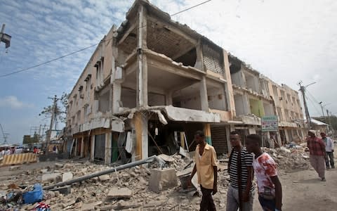 Men walk near destroyed buildings as thousands of Somalis gathered to pray at the site of the country's deadliest attack and to mourn the hundreds of victims, at the site of the attack in Mogadishu - Credit: AP