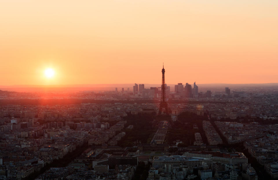 The sun sets behind the Eiffel Tower and the skyscrapers of La Defense business district in Paris, France.