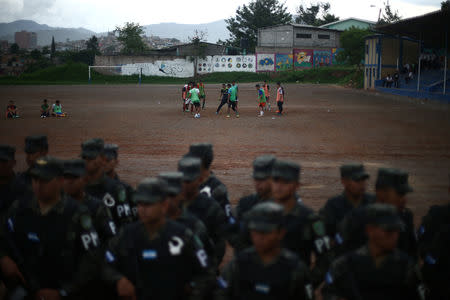 Men play soccer as soldiers line up in a neighbourhood occupied by gangs known as El Hoyo in Tegucigalpa, Honduras, June 13, 2018. REUTERS/Edgard Garrido