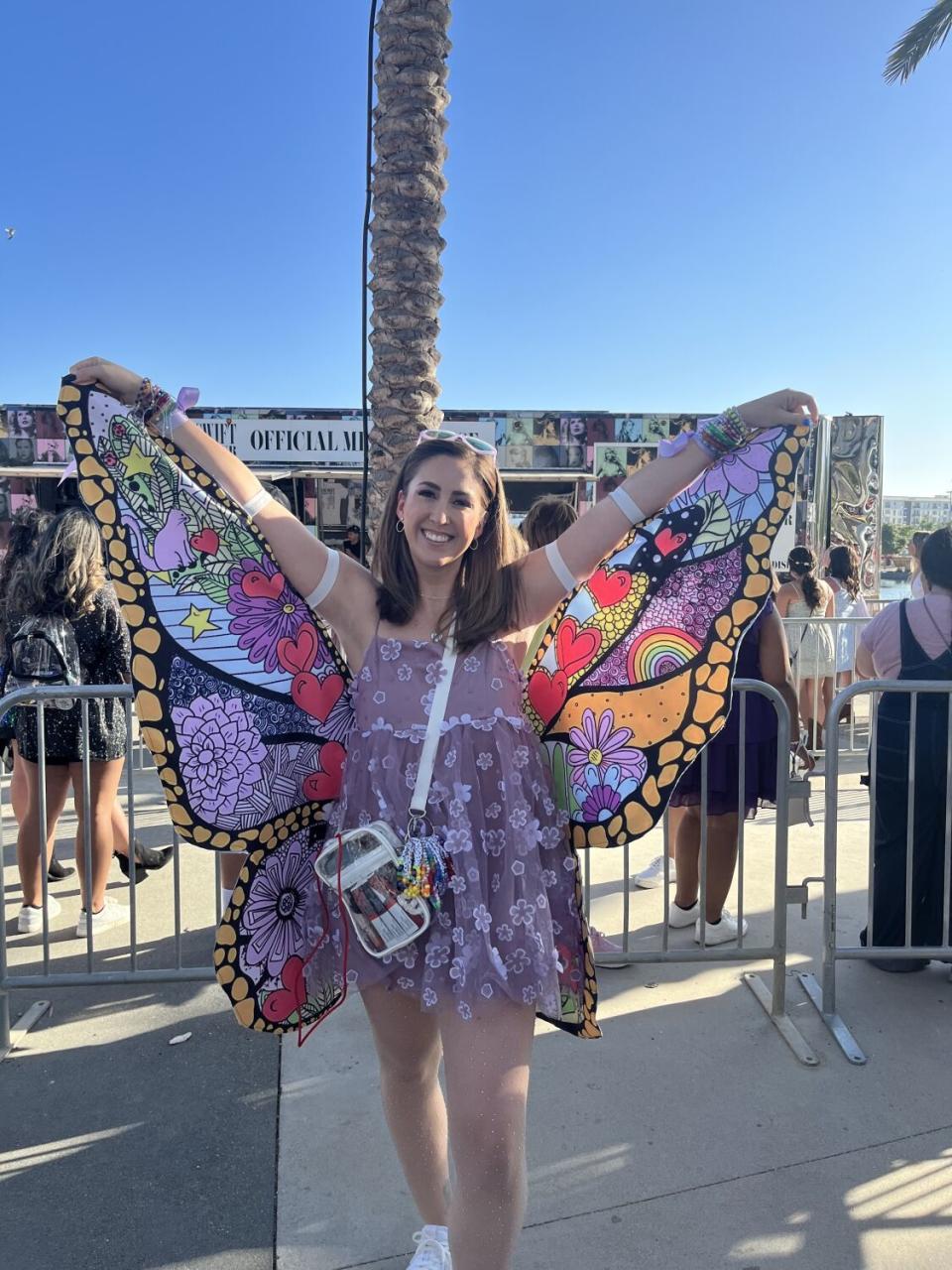 A woman in a short purple flowered dress holds up butterfly wings.