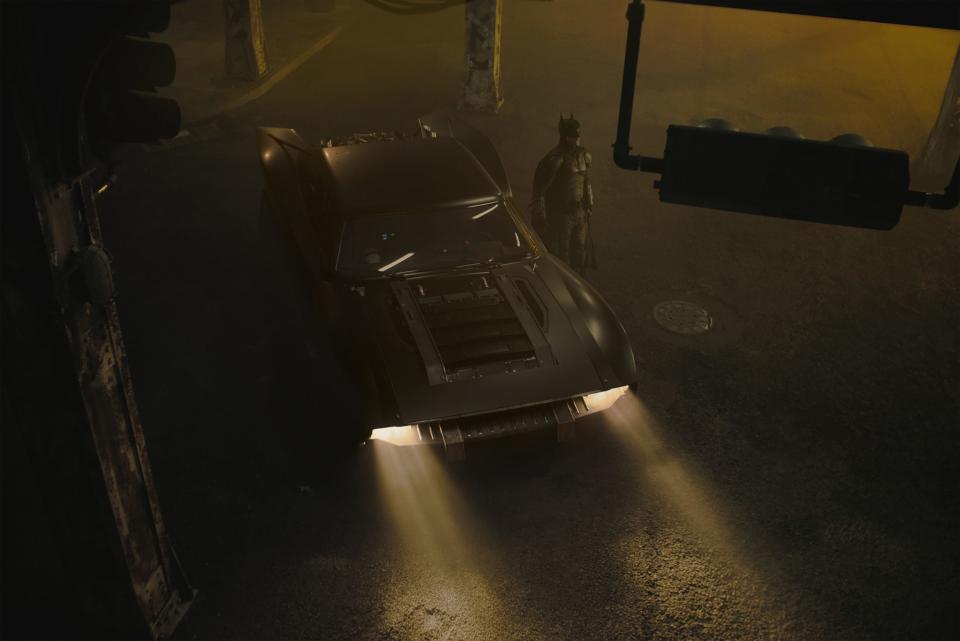 Batman standing next to the Batmobile