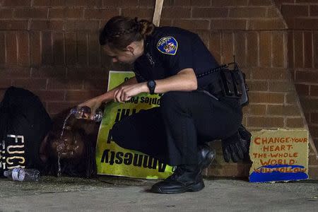 A police officer douses a man, who was hit by pepper spray after defying a curfew, with water as he lies detained in west Baltimore, Maryland May 2, 2015. REUTERS/Adrees Latif