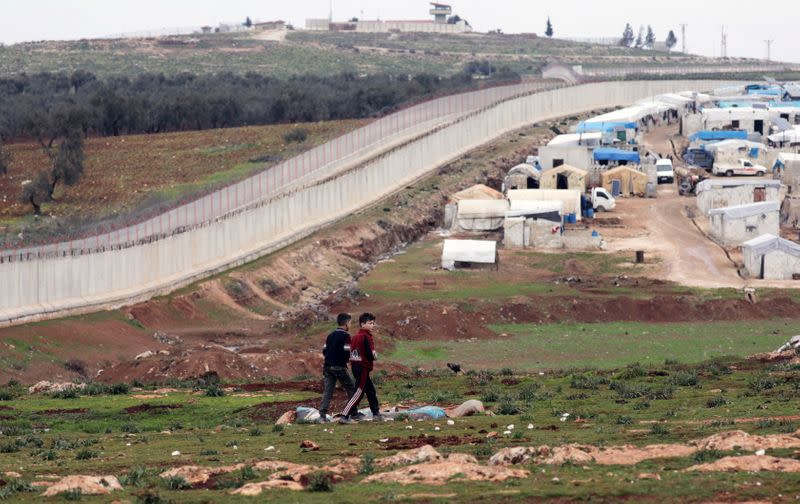 Internally displaced Syrian boys walk near the wall in Atmah IDP camp, located near the border with Turkey