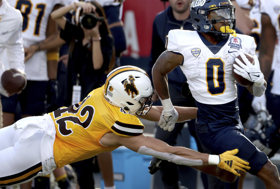 Toledo running back Jacquez Stuart (0) runs out of the arms of Wyoming safety Isaac White (42) on his way to a touchdown during the second quarter of the Arizona Bowl NCAA college football game Saturday, Dec. 30, 2023, in Tucson, Ariz. (Kelly Presnell/Arizona Daily Star via AP)