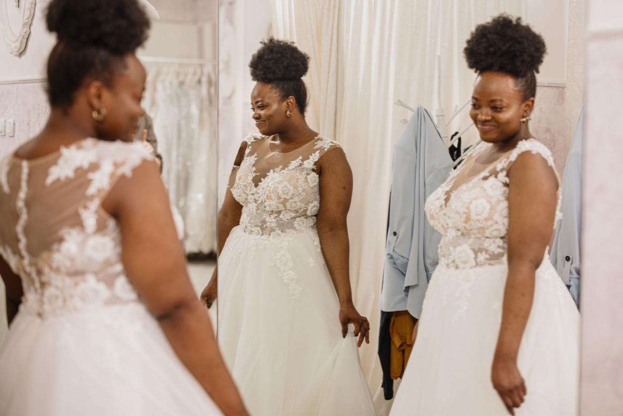 The future bride looks around the shop and tries on wedding dresses in the presence of her best friends. Lifestyle shopping concept, post-Covid-19 era