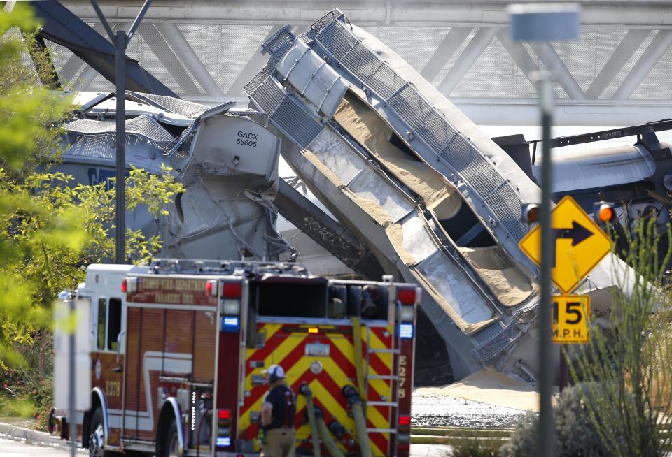 A derailed freight train hangs from a collapsed bridge Wednesday, July 29, 2020, in Tempe, Ariz. Officials say a freight train traveling on the bridge that spans a lake in the Phoenix suburb has derailed, setting the bridge ablaze and partially collapsing the structure. (AP Photo/Ross D. Franklin)