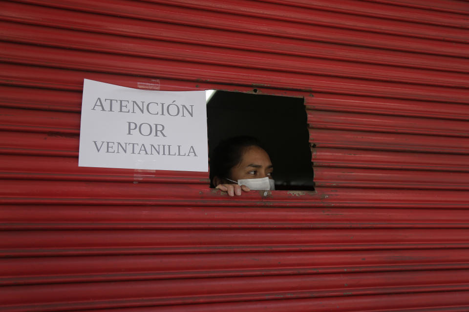 An employee waits on a customer via window service amid new lockdown restrictions due to the increase in COVID-19 infections, in Quito, Ecuador, Saturday, April 24, 2021. (AP Photo/Dolores Ochoa)